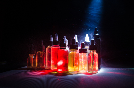 Vape concept. Smoke clouds and vape liquid bottles on dark background. Light effects. Useful as background or vape advertisement or vape background.の写真素材
