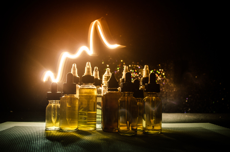 Vape concept. Smoke clouds and vape liquid bottles on dark background. Light effects. Useful as background or vape advertisement or vape background.の写真素材