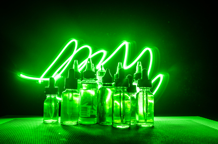 Vape concept. Smoke clouds and vape liquid bottles on dark background. Light effects. Useful as background or vape advertisement or vape background.の写真素材