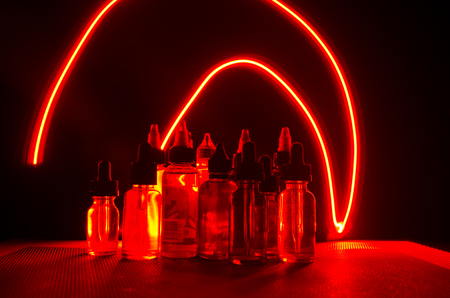 Vape concept. Smoke clouds and vape liquid bottles on dark background. Light effects. Useful as background or vape advertisement or vape background.の写真素材