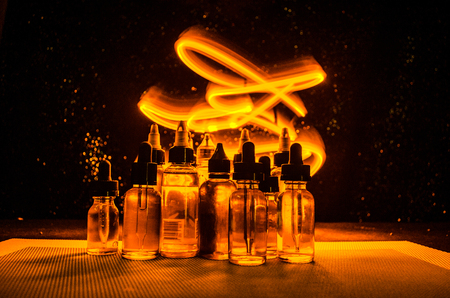Vape concept. Smoke clouds and vape liquid bottles on dark background. Light effects. Useful as background or vape advertisement or vape background.の写真素材