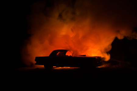 Burning car on a dark background. Car catching fire, after act of vandalism or road indicent. Burning vintage car nightshotの写真素材