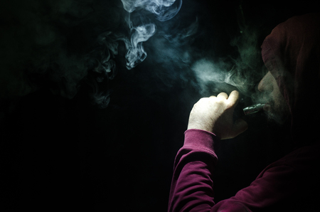 Vaping man holding a mod. A cloud of vapor. Black background. Vaping an electronic cigarette with a lot of smoke. Vape conceptの写真素材
