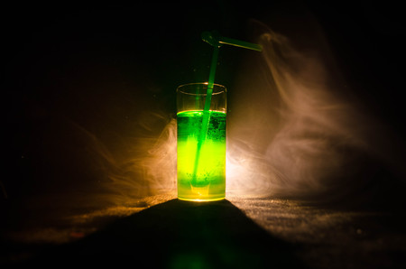 Glass of green cocktail with straw on dark background with smoke and backlights. Colorful coctailの写真素材