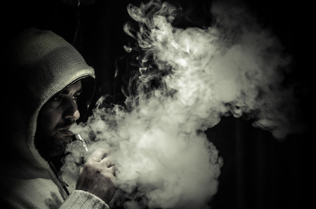 Vaping man holding a mod. A cloud of vapor. Black background. Vaping an electronic cigarette with a lot of smoke. Vape conceptの写真素材