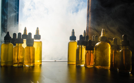 Vape concept. Smoke clouds and vape liquid bottles on window with sunlight on background. Light...