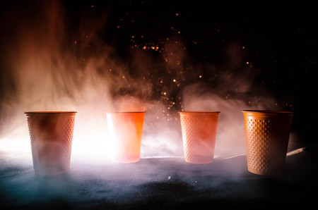 Stack of orange plastic cups with straw on dark background with smokeの写真素材