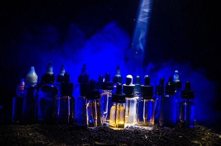 Vape concept. Smoke clouds and vape liquid bottles on dark background. Light effects. Useful as background or vape advertisement or vape background.の写真素材