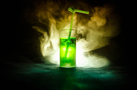 Glass of green cocktail with straw on dark background with smoke and backlights. Colorful coctailの写真素材