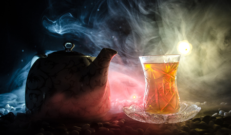 Turkish Azerbaijan tea in traditional glasse and pot on black background with lights and smoke. Eastern tea concept. Armudu traditional cupの写真素材