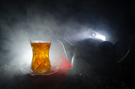 Turkish Azerbaijan tea in traditional glasse and pot on black background with lights and smoke. Eastern tea concept. Armudu traditional cupの写真素材