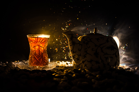Turkish Azerbaijan tea in traditional glasse and pot on black background with lights and smoke. Eastern tea concept. Armudu traditional cupの写真素材