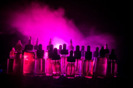 Vape concept. Smoke clouds and vape liquid bottles on dark background. Light effects. Useful as background or vape advertisement or vape background.の写真素材