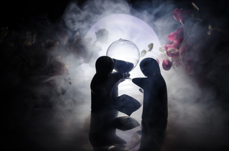 Two doll hugging on table with flowers and moon decoration Lighted background with smoke.Love concept. Greeting or gift card design idea. Silhouette of hugging coupleの写真素材