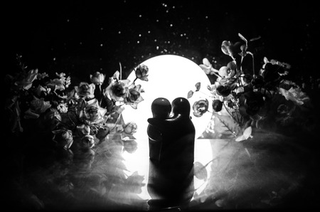 Two doll hugging on table with flowers and moon decoration Lighted background with smoke.Love concept. Greeting or gift card design idea. Silhouette of hugging coupleの写真素材