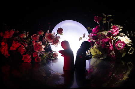 Two doll hugging on table with flowers and moon decoration Lighted background with smoke.Love concept. Greeting or gift card design idea. Silhouette of hugging coupleの写真素材