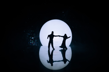 Silhouettes of toy couple dancing under the Moon at night. Figures of man and woman in love dancing at moonlight with fogの写真素材