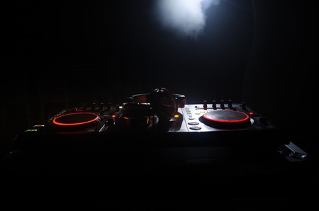DJ Spinning, Mixing, and Scratching in a Night Club, Hands of dj tweak various track controls on dj's deck, strobe lights and fog, selective focus, close upの写真素材