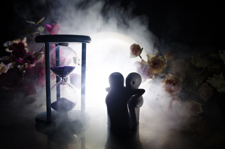 Two doll hugging on table with flowers and moon decoration Lighted background with smoke.Love concept. Greeting or gift card design idea. Silhouette of hugging coupleの写真素材