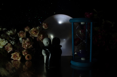 Two doll hugging on table with flowers and moon decoration Lighted background with smoke.Love concept. Greeting or gift card design idea. Silhouette of hugging coupleの写真素材