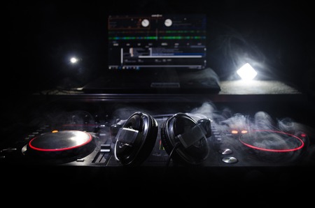 DJ Spinning, Mixing, and Scratching in a Night Club, Hands of dj tweak various track controls on dj's deck, strobe lights and fog, selective focus, close upの写真素材