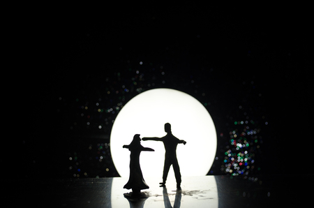 Silhouettes of toy couple dancing under the Moon at night. Figures of man and woman in love dancing at moonlight with fogの写真素材