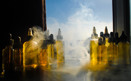 Vape concept. Smoke clouds and vape liquid bottles on window with sunlight on background. Light effects. Useful as background or vape advertisement or vape background.の写真素材