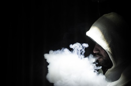 Vaping man holding a mod. A cloud of vapor. Black background. Vaping an electronic cigarette with a...