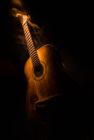 Music concept. Acoustic guitar isolated on a dark background under beam of light with smoke with copy space. Guitar Strings, close up. Selective focus. Fire effects. Surreal guitarの写真素材