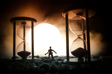 Time concept. Silhouette of a man standing between hourglasses with smoke and lights on a dark...