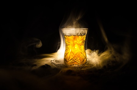 Turkish Azerbaijan tea in traditional glasse and pot on black background with lights and smoke. Eastern tea concept. Armudu traditional cupの写真素材