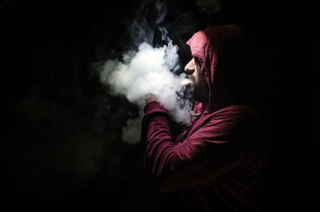 Vaping man holding a mod. A cloud of vapor. Black background. Vaping an electronic cigarette with a lot of smoke. Vape conceptの写真素材