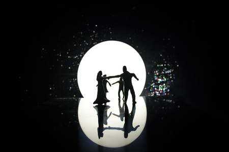 Silhouettes of toy couple dancing under the Moon at night. Figures of man and woman in love dancing at moonlight with fogの写真素材