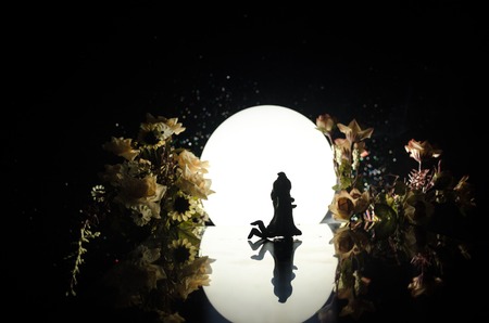 Silhouettes of toy couple dancing under the Moon at night. Figures of man and woman in love dancing at moonlight with fogの写真素材