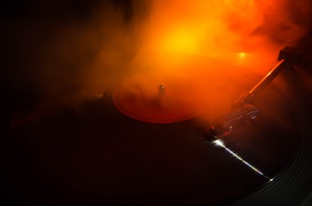 Turntable vinyl record player. Retro audio equipment for disc jockey. Sound technology for DJ to mix & play music. Vinyl record being played against burning fire background with smokeの写真素材