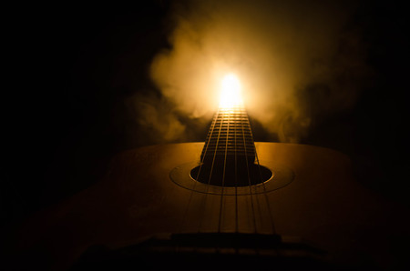 Music concept. Acoustic guitar isolated on a dark background under beam of light with smoke with copy space. Guitar Strings, close up. Selective focus. Fire effects. Surreal guitarの写真素材