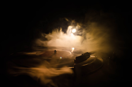 Turntable vinyl record player. Retro audio equipment for disc jockey. Sound technology for DJ to mix & play music. Vinyl record being played against burning fire background with smokeの写真素材