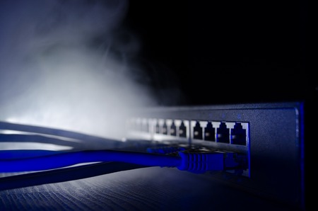 Network switch and ethernet cables, symbol of global communications. Colored network cables on dark background with lights and smoke. Selective focus. Network internet concept backgroundの写真素材