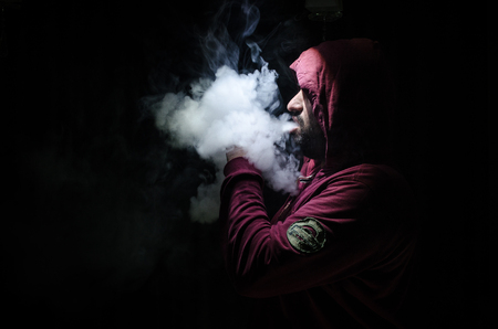 Vaping man holding a mod. A cloud of vapor. Black background. Vaping an electronic cigarette with a lot of smoke. Vape conceptの写真素材