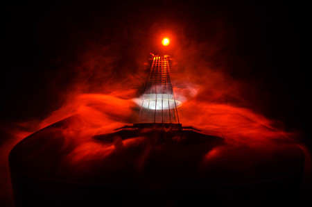 Music concept. Acoustic guitar isolated on a dark background under beam of light with smoke with copy space. Guitar Strings, close up. Selective focus. Fire effects. Surreal guitarの写真素材