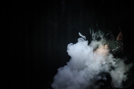 Vaping man holding a mod. A cloud of vapor. Black background. Vaping an electronic cigarette with a lot of smoke. Vape conceptの写真素材