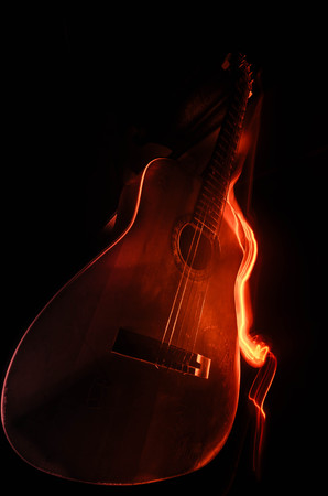 Music concept. Acoustic guitar isolated on a dark background under beam of light with smoke with copy space. Guitar Strings, close up. Selective focus. Fire effects. Surreal guitarの写真素材