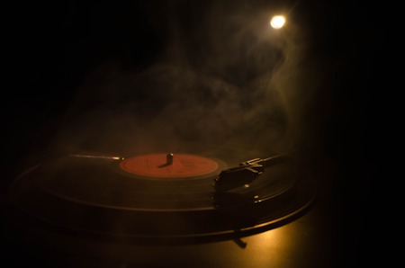 Turntable vinyl record player. Retro audio equipment for disc jockey. Sound technology for DJ to mix & play music. Vinyl record being played against burning fire background with smokeの写真素材