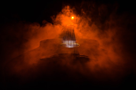 Music concept. Acoustic guitar isolated on a dark background under beam of light with smoke with copy space. Guitar Strings, close up. Selective focus. Fire effects. Surreal guitarの写真素材