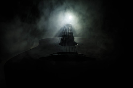 Music concept. Acoustic guitar isolated on a dark background under beam of light with smoke with copy space. Guitar Strings, close up. Selective focus. Fire effects. Surreal guitarの写真素材