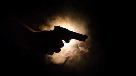 Male hand holding gun on black background with smoke ( yellow orange red white ) colored back lightsの写真素材