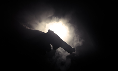 Male hand holding gun on black background with smoke ( yellow orange red white ) colored back lightsの写真素材