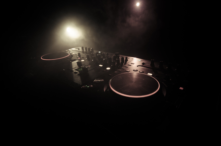 DJ Spinning, Mixing, and Scratching in a Night Club, Hands of dj tweak various track controls on dj's deck, strobe lights and fog, selective focus, close upの写真素材