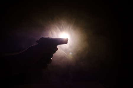 Male hand holding gun on black background with smoke ( yellow orange red white ) colored back lightsの写真素材