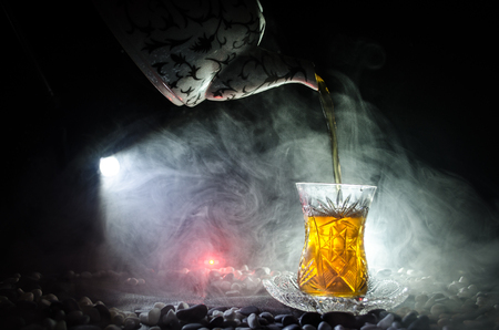 Turkish Azerbaijan tea in traditional glasse and pot on black background with lights and smoke. Eastern tea concept. Armudu traditional cupの写真素材
